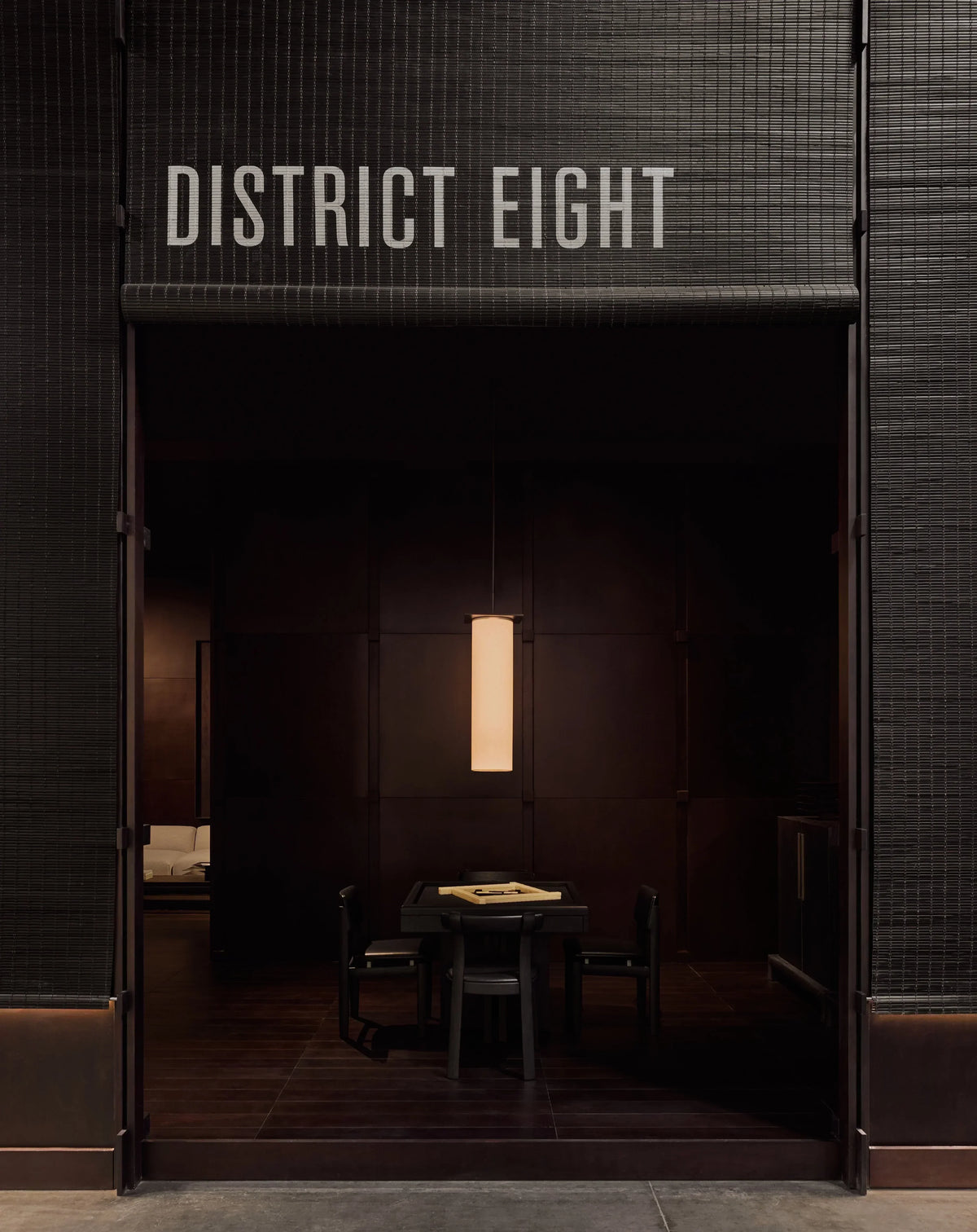 Interior view of District Eight Milan Design Week booth with bamboo curtains, textured walls and warm minimal lighting