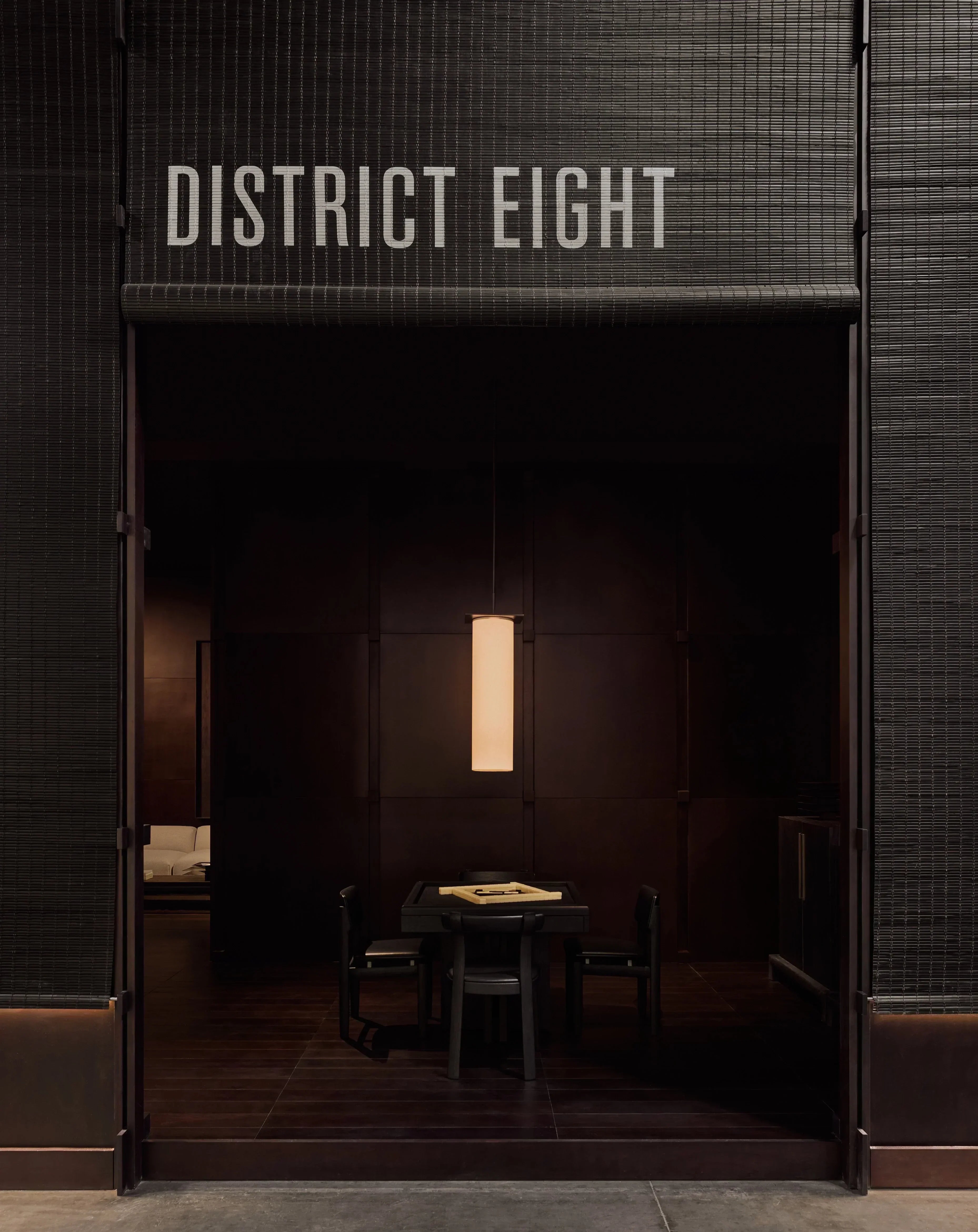 Interior view of District Eight Milan Design Week booth with bamboo curtains, textured walls and warm minimal lighting